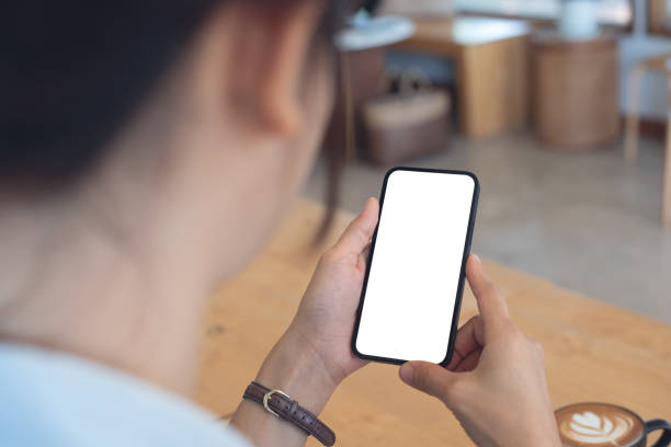 istock Mockup, woman's hands holding mobile phone with blank screen in coffee shop, over shoulder view 2014487535