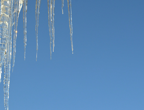 A view through a row of long hanging icicles on a mountain house looking high over a winter landscape.