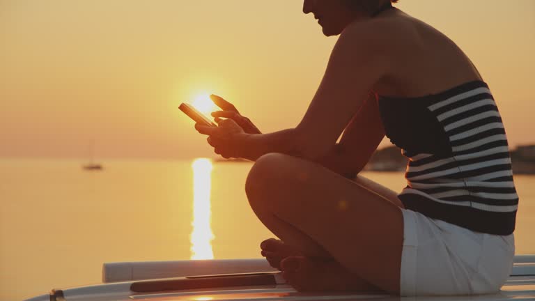 SLO MO Shot of Woman Using Smartphone While Sitting on Camping Van by Sea at Sunset