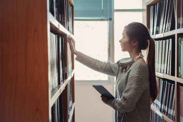 istock Young asian female college student taking book from shelf in library. 2014561387