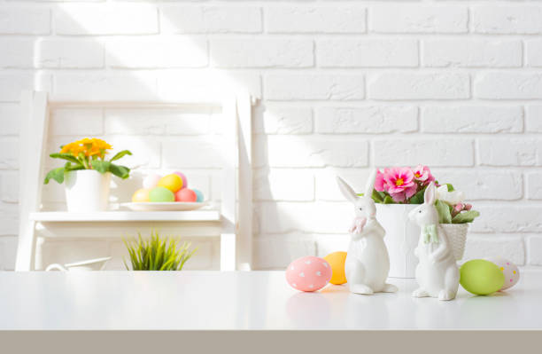 istock Easter bunnies and painted eggs on table over background of white brick wall with decorated shelf 2014564516
