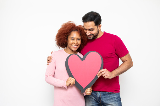 Love and romance concept. Studio shot of a happy heterosexual couple standing together and holding a large heart shape. They are casually dressed.