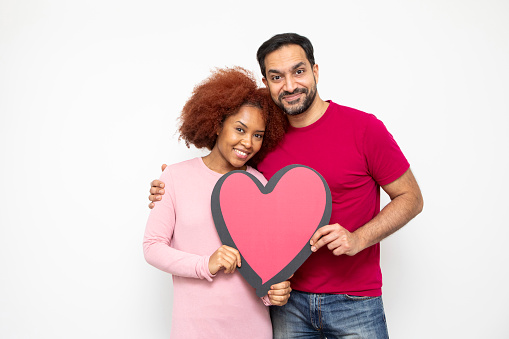 Love and romance concept. Studio shot of a happy heterosexual couple standing together and holding a large heart shape. They are casually dressed.