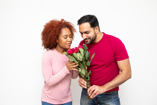 Love and romance concept. Studio shot of a happy heterosexual couple standing together and holding a bunch of red roses. They are casually dressed.