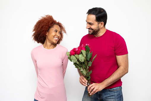 Love and romance concept. Studio shot of a happy heterosexual couple standing together and holding a bunch of red roses. They are casually dressed.