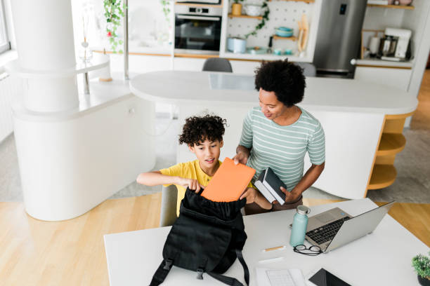 istock Schoolboy packing his backpack with school supplies with a help of her mother 2014609549