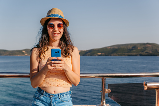 Young woman using phone on the boat in Parga in Greece.