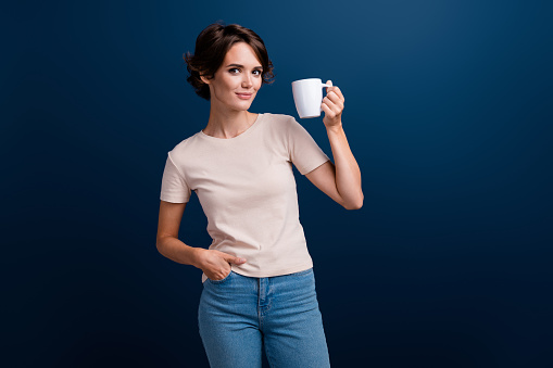 Beautiful shorthaired woman standing in living room at home, she is holding a cup of coffee.