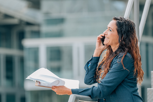 business woman talking on mobile phone on the street with documents