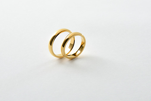 Detail of engagement gold rings standing parallel next to each other isolated on white textured background. Elevated view.