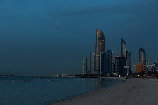 Public beach with high-rises and buildings of the city of Abu Dhabi, UAE late evening after sunset