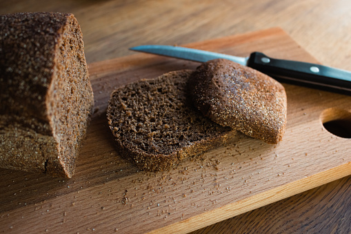 Rye bread with knife on wooden board. Wheat bread slices on cutting board. Bakery products. Crusty grain bread on table. Dinner concept. Healthy eating lifestyles. Fresh cereal loaf. Fresh food concept.