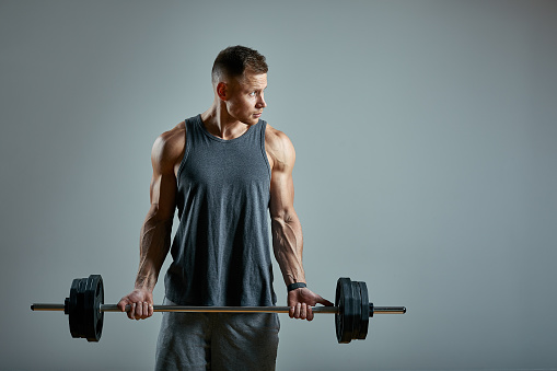 Man doing back workout, barbell row in studio over gray background. Copy space, sport banner for advertising