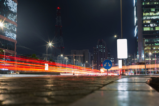 Night traffic street with red lights, billboard, buildings and cell tower at night in Abu Dhabi. Night life