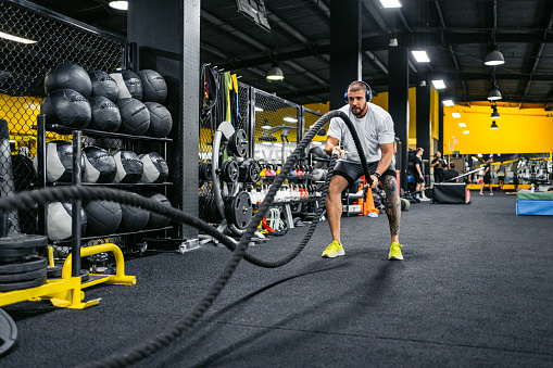 Handsome young man training with battle ropes while listening to music via headphones in the gym in Kuwait City.