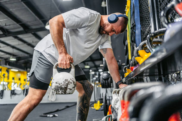 young man training with a kettlebell while listening to music in the gym - hand weight audio photos et images de collection