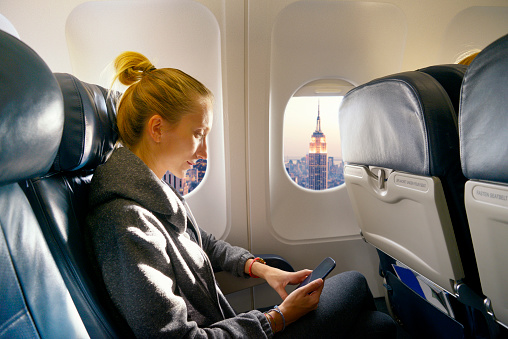 Young woman looking phone  in airplane before landing in NYC