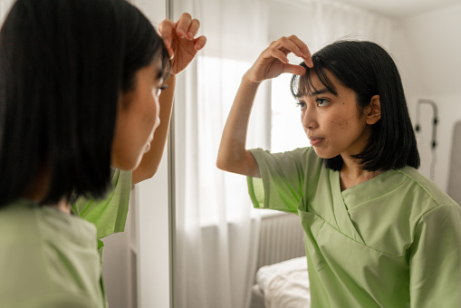 Woman fixing her hair in front of the mirror in the morning. Part of a series with an asian woman getting dressed in her medical scrubs in front of the mirror in her bedroom.