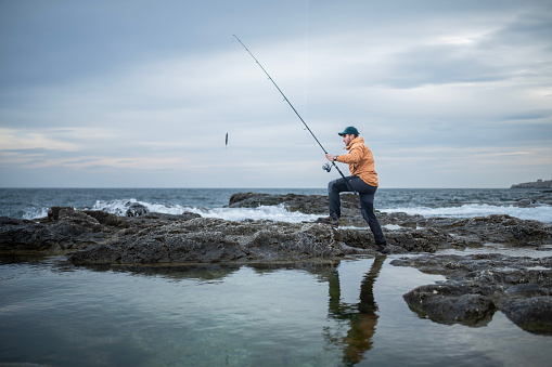 Fisherman pulling the rod after catching a fish on a shore fishing adventure.