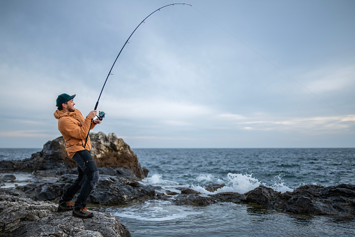 Fisherman pulling the rod after catching a fish on a shore fishing adventure.