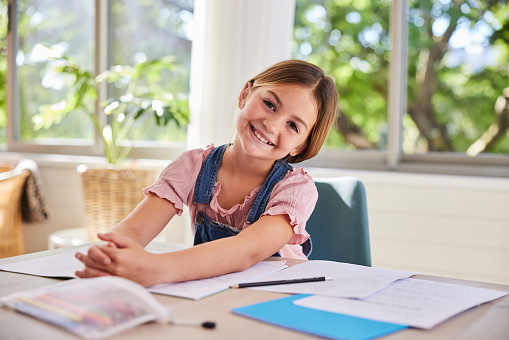 Portrait of a smiling young girl doing her elementary school homework at a desk at home