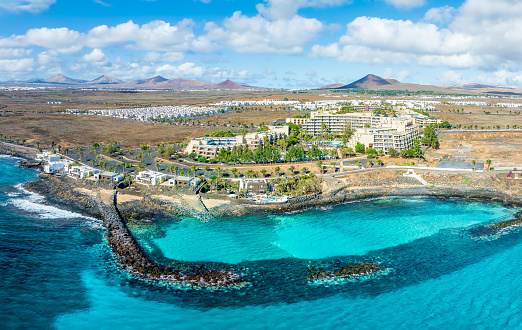 Overlook the serene Playa El Ancla in Costa Teguise, Lanzarote, where crystal-clear waters and volcanic landscapes offer a picturesque retreat.
