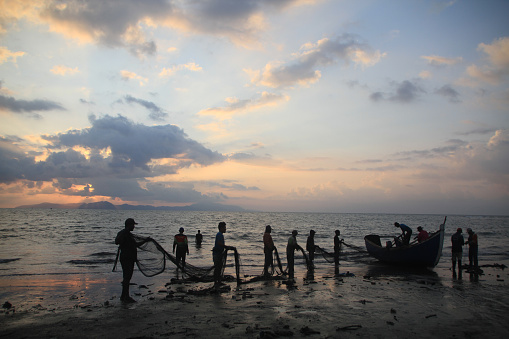 On the coast of Banda Aceh on 08/19/2020 . a group of fishermen from the Javanese village skillfully cleaned their nets. Amidst the sunset ambiance, they employed the traditional method of shore seine to catch fish. Their hands moved skillfully and systematically, clearing debris and repairing the nets. The twilight light enhanced their silhouettes, creating a beautiful portrayal of fishermen's lives deeply intertwined with the sea.