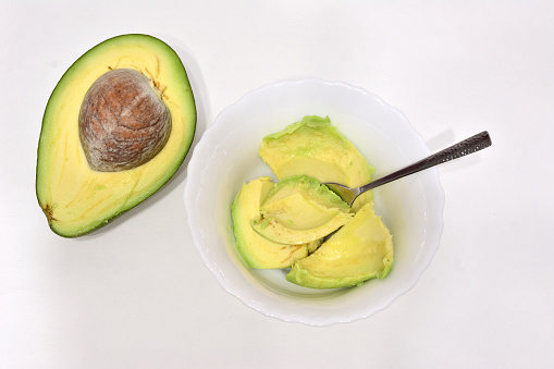 halved avocado with smashed avocado in bowl top view