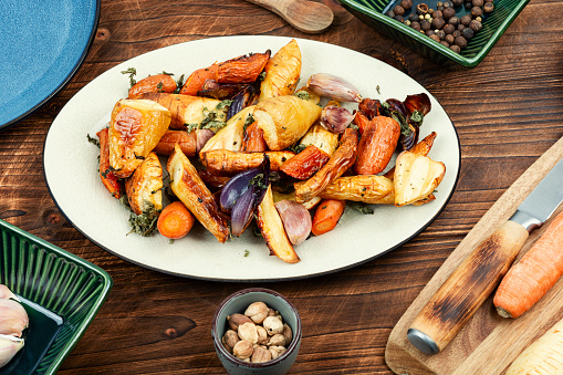 Healthy homemade roasted parsnip root, carrots and garlic on old rustic wooden table.