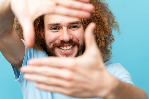 Happy man with curly hair making a frame with his hands in front of his face