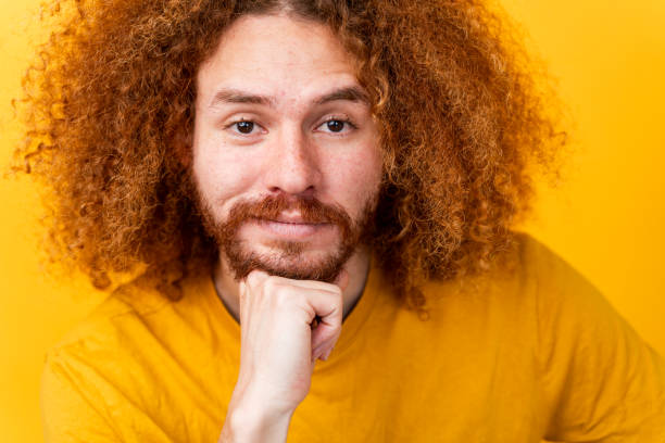 Man with curly hair deep in thought, hand resting on chin, yellow background