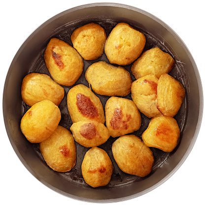Bunch of delicious freshly oven baked golden crunchy roasted potatoes halves, oven baked in round vintage non stick baking pan, viewed directly above, isolated on white background.