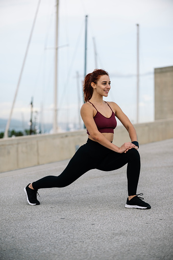 Woman stretching during an outside fitness training session. Happy lady smiling in athletic exercise warming up for running.
