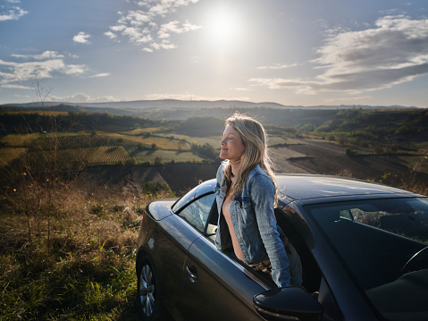 Carefree woman enjoying in fresh autumn air with her eyes closed through car window. Photographed in medium format. Copy space.
