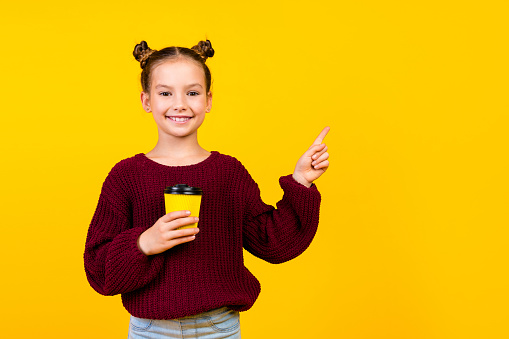 Portrait of small positive person beaming smile hold coffee cup indicate finger empty space isolated on yellow color background.