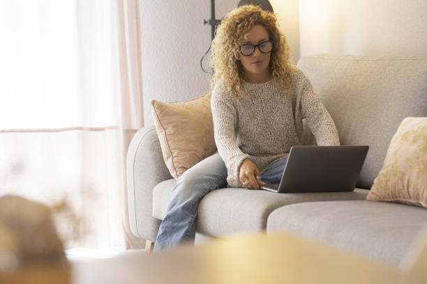 istock One woman at home using laptop sitting on the sofa in comfortable relaxation indoor leisure activity. People working online with computer. Curly adult female use technology and connection wireless 2014997669