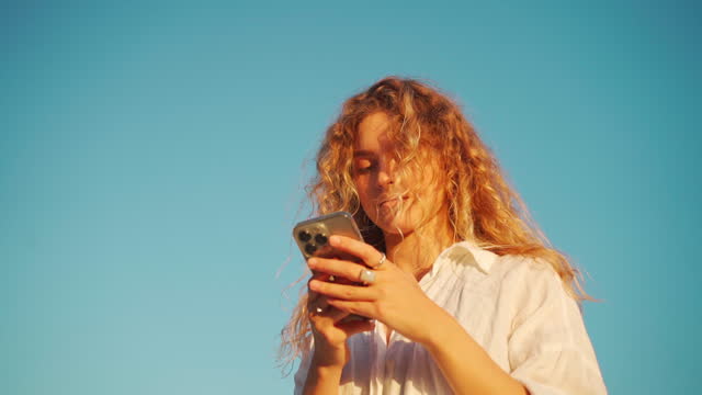 Woman text messaging via smartphone against bright blue sky