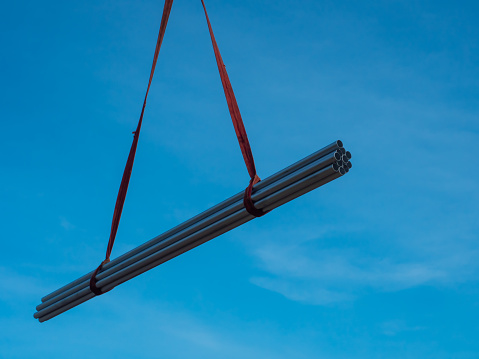 The bundle of pipes are lifted by the crane truck at construction site.