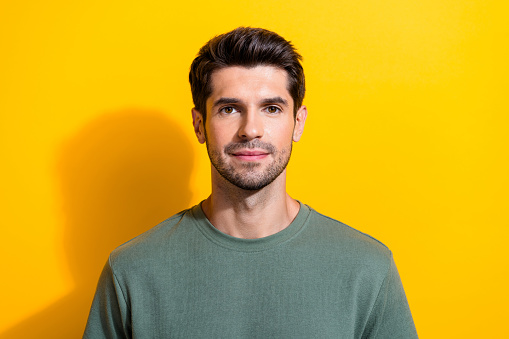 Photo of serious confident man with bristle stylish hairdo dressed khaki t-shirt look at camera isolated on yellow color background.