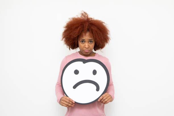 Sadness and disapproval concept - one young woman holding an anthropomorphic sad face. She is looking at the camera with an unhappy expression.