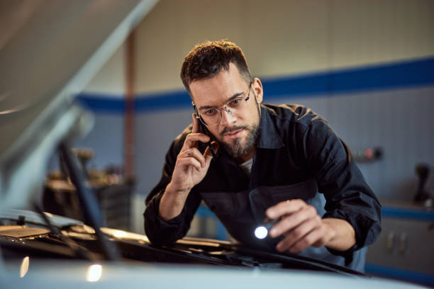 istock Focused man working as a mechanic, using a lamp and checking the car while making a phone call with a customer. 2015042058