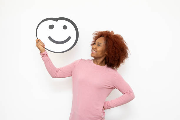 Happiness and approval concept - one young woman holding an anthropomorphic smiley face. She is looking to the side and smiling.