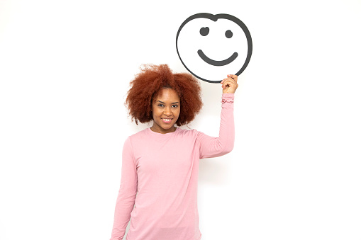 Happiness and approval concept - one young woman holding an anthropomorphic smiley face. She is looking at the camera and smiling.