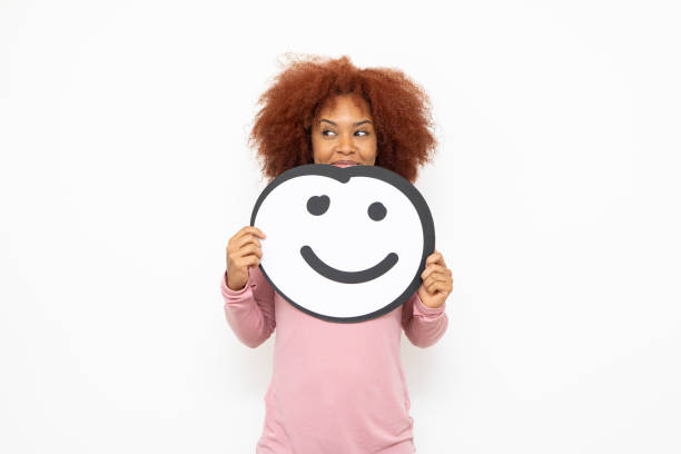 Happiness and approval concept - one young woman holding an anthropomorphic smiley face. She is looking to the side and smiling.