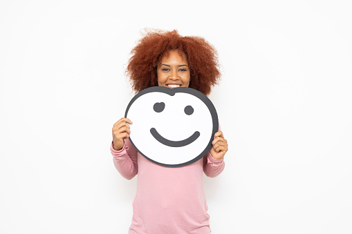Happiness and approval concept - one young woman holding an anthropomorphic smiley face. She is looking at the camera and smiling.