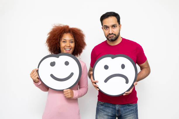 Approval and disapproval concept - male and female couple holding anthropomorphic faces. She is happy, he is sad.