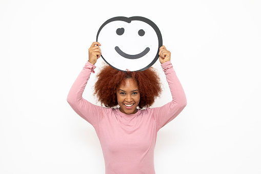 Happiness and approval concept - one young woman holding an anthropomorphic smiley face. She is looking at the camera and smiling.