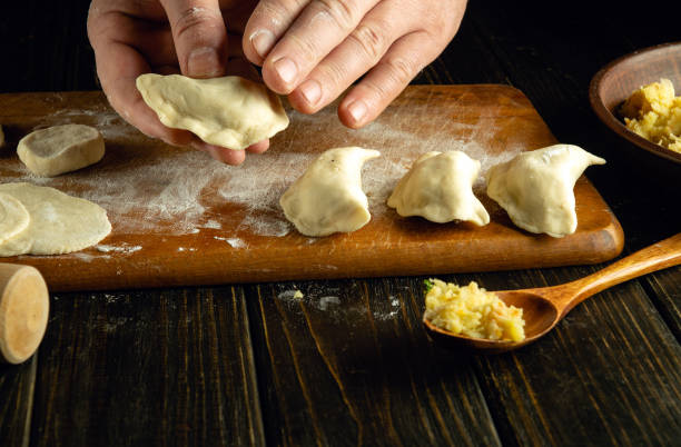 istock Men hands sculpting varenyky. Step-by-step process of making homemade dumplings stuffed with mashed potato on a dark table. Cooking process. Ukrainian cuisine 2015049064