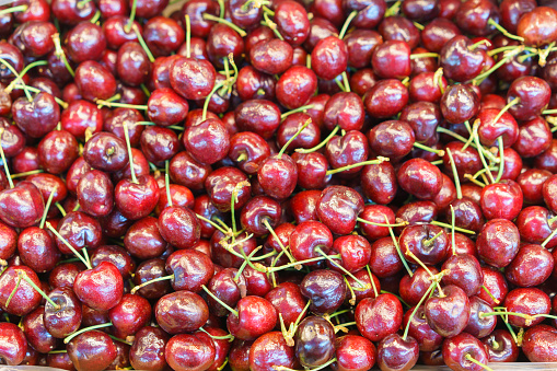 A large heap of shiny, ripe cherries with stems, offering a fresh and juicy texture, displayed at a fruit market