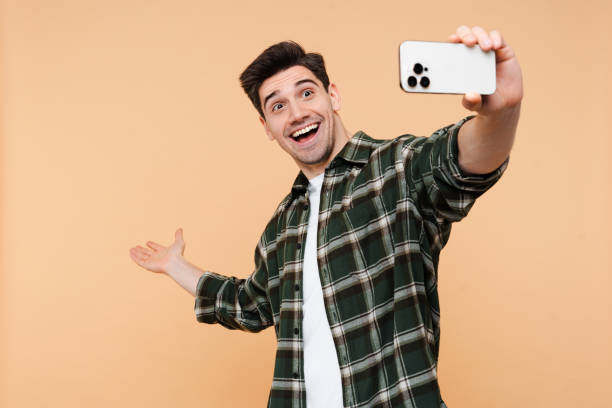 Happy amazed guy taking selfie gesturing hand looking at camera on mobile phone